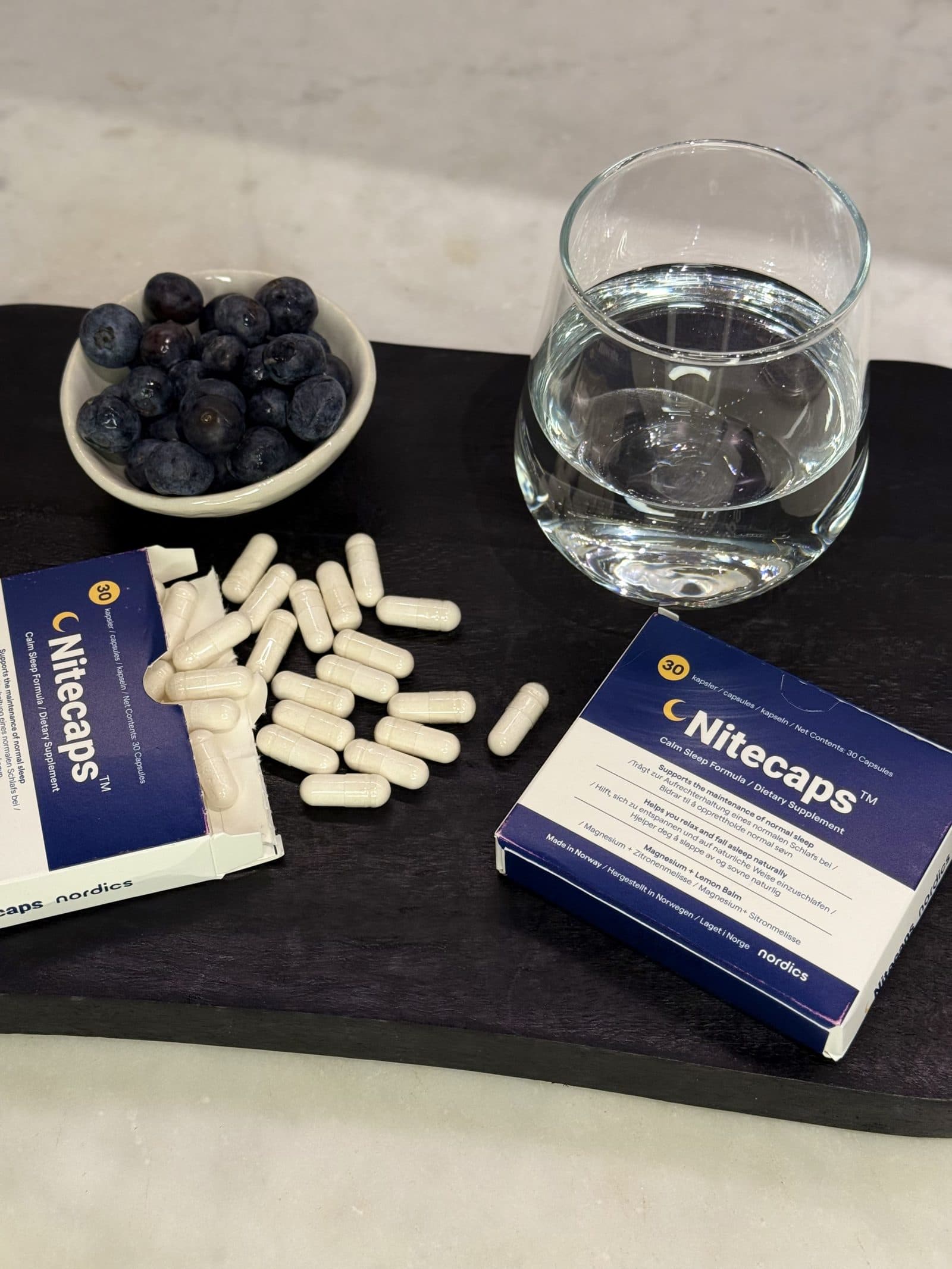 Integratore alimentare NiteCaps senza melatonina, con capsule e un bicchiere d’acqua.